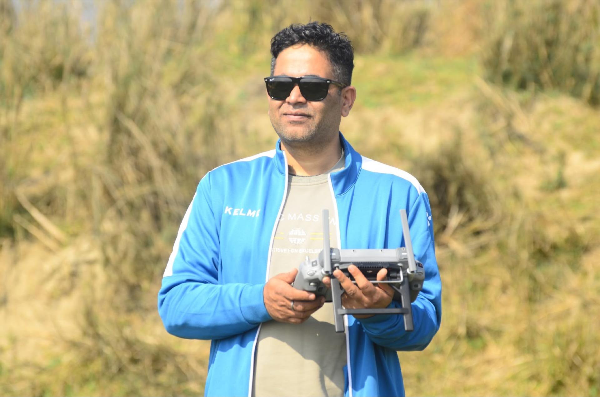 Survey pilot operating a drone controller beside tall riverbank grass