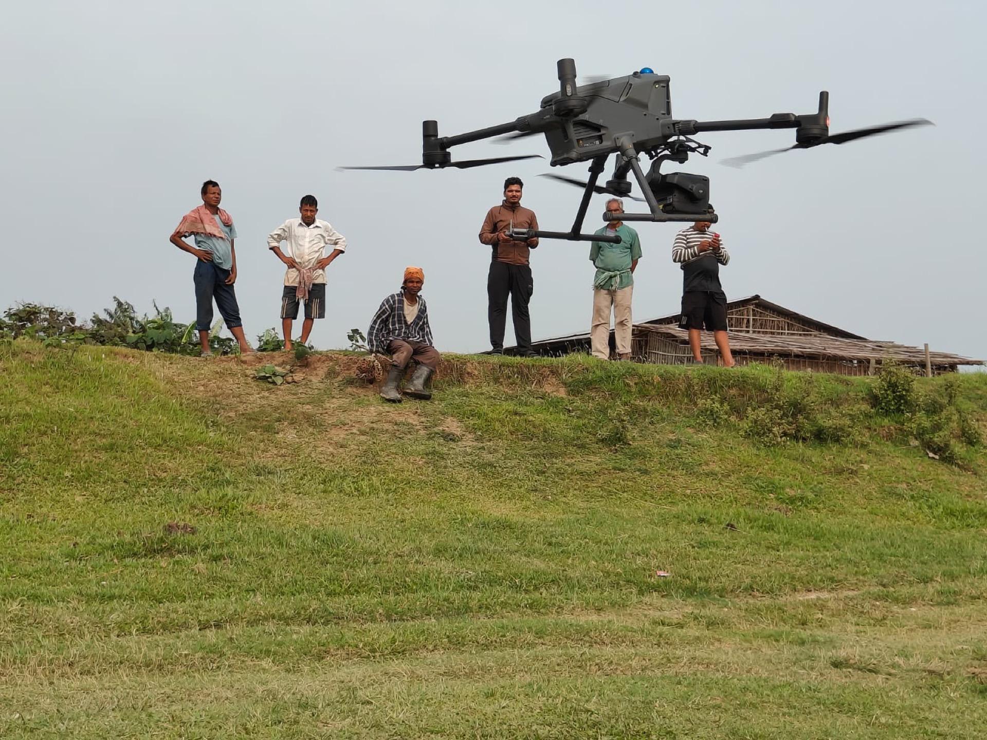 Large survey drone lifting off from a grass embankment while the field crew observes